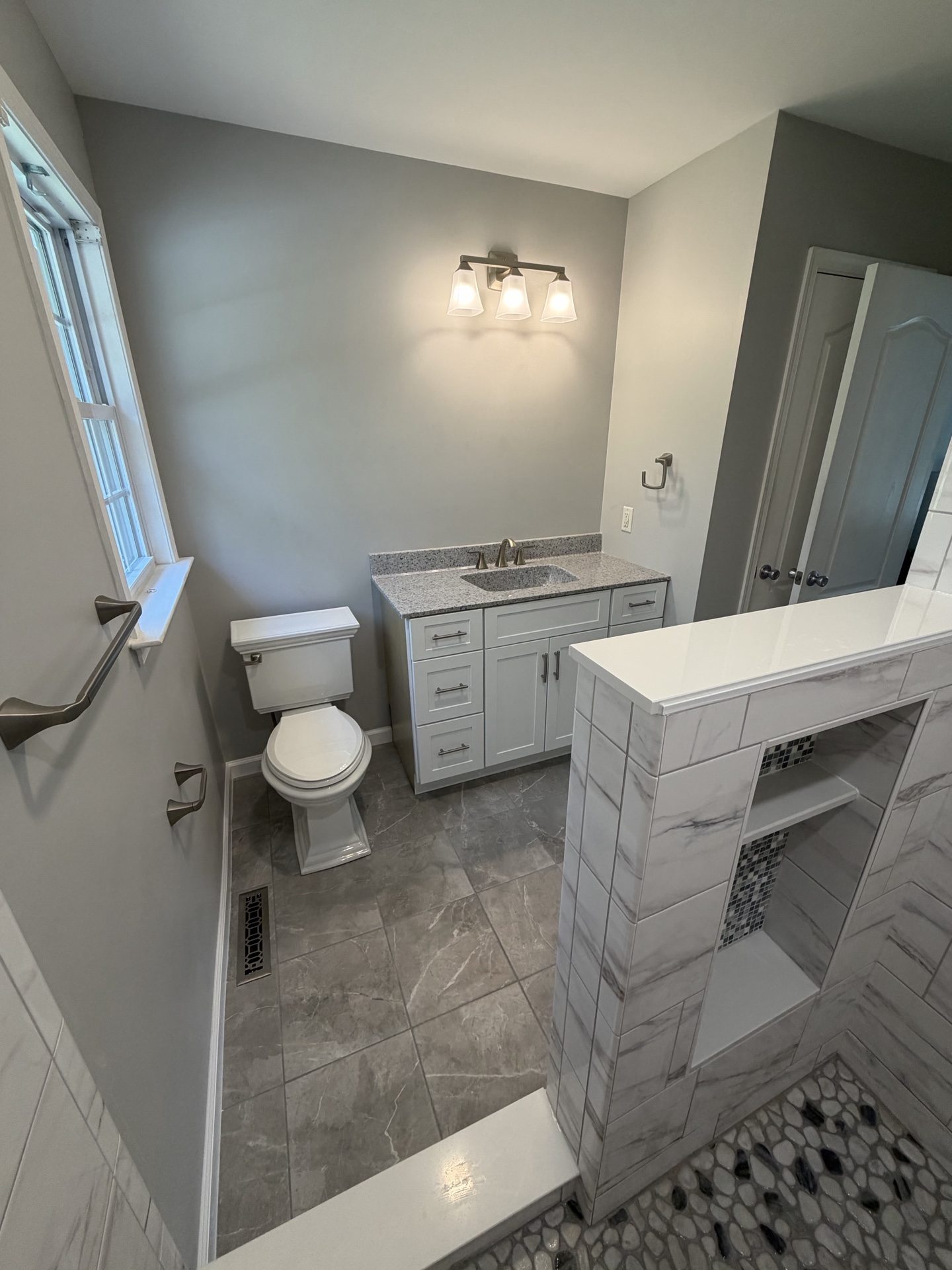 Full view of a finished Schuylkill County bathroom remodel: white floating vanity, gray tile floor, walk-in shower.