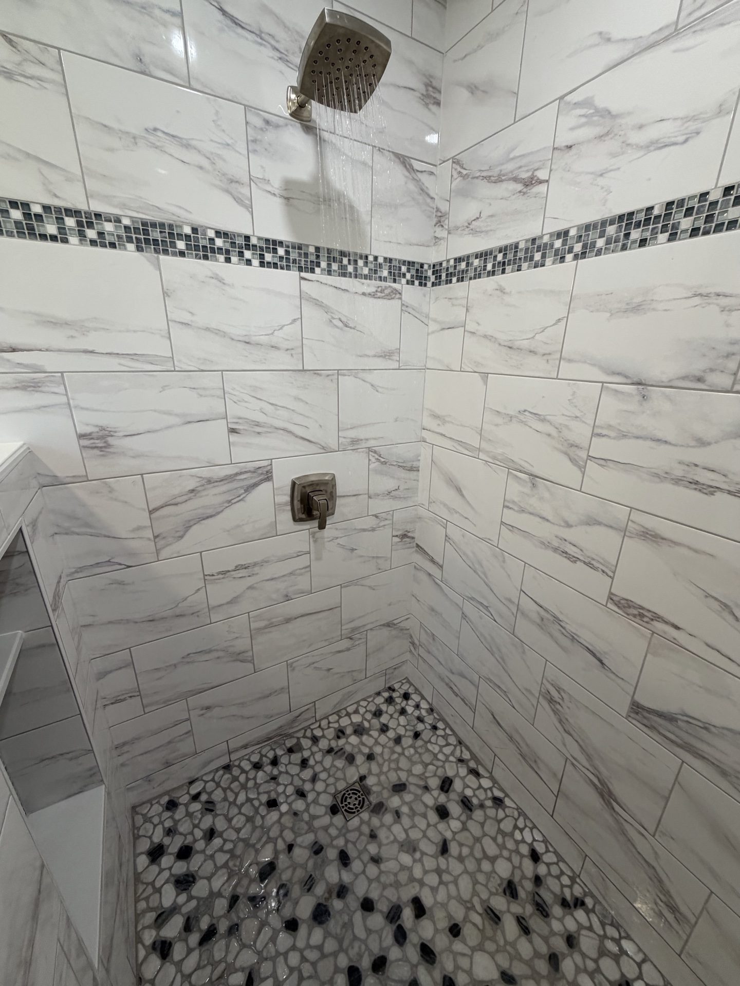 Marble-tile shower interior with pebble-tile floor in a Schuylkill County bathroom remodel &mdash; close look at hand-set tile work.